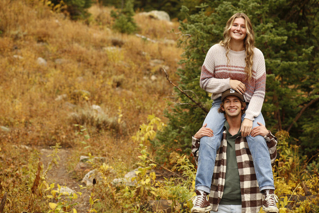 Man and Woman in brown standing in front of a yellow flower covered hill.