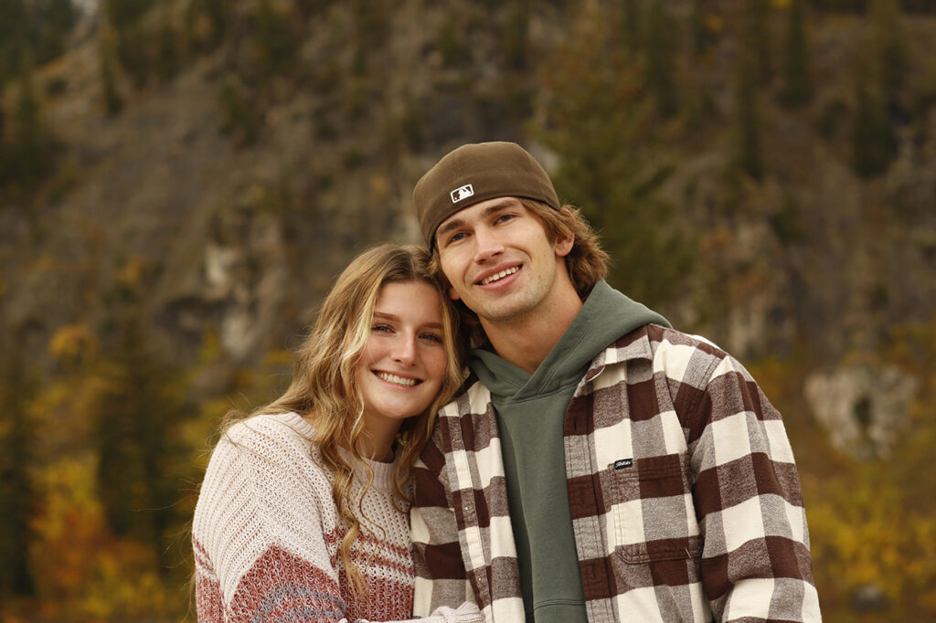 Male and Female wearing brown standing in front of a lake and mountains